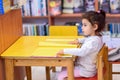 Little Girl Indoors In Front Of Books. Cute Young Toddler Sitting On A Chair Near Table and Reading Book. Royalty Free Stock Photo