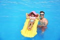 Little girl on inflatable mattress with father in pool