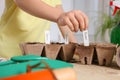 Little girl inserting cards with names of vegetable seeds into peat pots indoors, closeup
