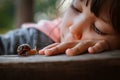 Little girl intently watching small snail crawling along wooden bench while spending time in nature Royalty Free Stock Photo