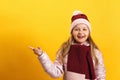 Little girl in a jacket, scarf and hat on a yellow background. The child shows the index finger to the side Royalty Free Stock Photo