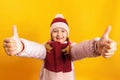 Little girl in a jacket, scarf and hat on a yellow background. The child shows a thumb up with two hands Royalty Free Stock Photo