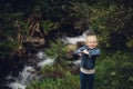 A little girl in jeans clothes, stands against the backdrop of a mountain river with stones and a forest Royalty Free Stock Photo