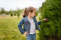 Little girl in jeans jacket posing outdoors in spring park touching green bush leaves. Interested clever child, exploring