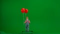 Little girl in jeans overall and ponytail with red helium balloons walking on chroma key green screen isolated