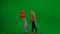 Little girl in jeans overall with red helium balloons together with woman walking on chroma key green screen isolated