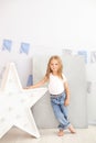 Little girl in jeans and a white T-shirt stands by the luminous star of the lamp. Large decorative retro star. Christmas, New Year