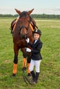 Little girl jockey lead horse by its reins across country in professional outfit Royalty Free Stock Photo