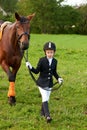 Little girl jockey lead horse by its reins across country in professional outfit Royalty Free Stock Photo