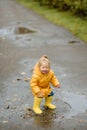 A little girl is jumping in a puddle in yellow rubber boots and a waterproof raincoat.