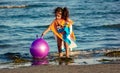 Little girl just out of the sea with her pom pom ball and a towel on her back to dry off.