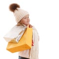 A little girl in a knitted hat with a pompon, scarf and sweater, is holding multicolored paper bags. Isolated on white background Royalty Free Stock Photo