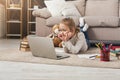 Cute little girl doing homework on laptop, lying on floor Royalty Free Stock Photo