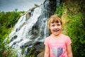 Little girl laughs against the waterfall. A happy child is standing by the side of a bubbling river. A girl is smiling happily in