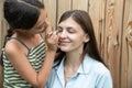 Little girl learn to do a makeup on her older sister, applying liquid tonal foundation on the face. Outdoor photo on