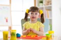 Little girl is learning to use colorful plasticine in well lit room near window