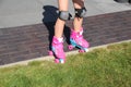 Little girl learns riding pink four-wheeled roller skates on the grass, knee pads, legs, close-up Royalty Free Stock Photo