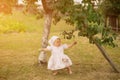 A little girl learns to walk unsteadily while standing under an apple tree