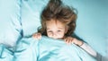 Little girl lies on a bed blue linens the top view hid under a blanket for fear Royalty Free Stock Photo