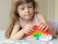 Little girl lies on the bed and plays with pop it in the shape of a rainbow, squashing bubbles with her fingers Royalty Free Stock Photo