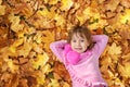 A little girl lies on the ground with orange maple leaves and smiling Royalty Free Stock Photo