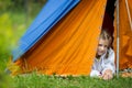 A little girl lies in an orange and blue tent on green grass Royalty Free Stock Photo