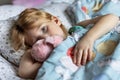 A little girl lies under a blanket with a toy dog getting ready for bed Royalty Free Stock Photo