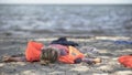 Little girl in life jacket lying on seashore, survivor of natural disaster flood