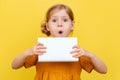 A little girl with light hair on a yellow background. Isolated. A child in a yellow dress makes notes on a book. Mockup. Royalty Free Stock Photo