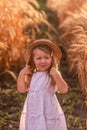 Little girl in a light pink sundress and a straw hat runs across a field of golden wheat and rye Royalty Free Stock Photo