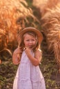 Little girl in a light pink sundress and a straw hat runs across a field of golden wheat and rye Royalty Free Stock Photo