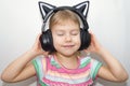 A little girl listens to music in funny headphones in the shape of cat ears. The concept of a happy child.