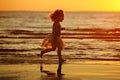 Little girl little girl in a skirt and striped sweater runs through the water, making a splash at sunset in summer Royalty Free Stock Photo