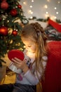 A little girl with long blonde hair opened a Christmas gift-a box with a light inside. New year, holiday decor, emotions. A gift f Royalty Free Stock Photo