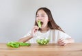 Little girl with long hair having fun eating green salad leaves, vegan vegetable salad sitting at the table