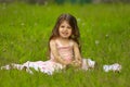 a little girl with long hair sits on the grass in the park in the summer Royalty Free Stock Photo