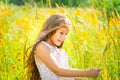 Little girl with long hair in a white dress rejoices in a field with flowers