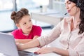 Little girl looking at busy mother in headset working with laptop Royalty Free Stock Photo