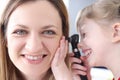 Little girl looking at ear of woman doctor with otoscope