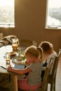 Little girl looking focused, using digital tablet pc while having breakfast or lunch, sitting together with her brother