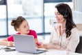 Little girl looking at happy mother in headset working with laptop Royalty Free Stock Photo