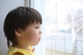 Little girl looking out the window longing for some sunshine. child sitting home at rainy day Royalty Free Stock Photo