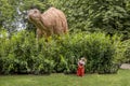 Little girl looking up at a big dinosaur, Girl in red dress, Brontosaurus dinosaur behind a big bush