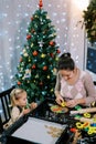 Little girl looks at her mother cutting out cookies with colorful cookie cutters on the table