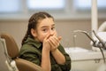 Little girl looks worried with fear closes mouth with handssitting in a dental chair