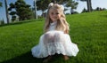 Little girl with loose hair in a white dress sits on the green grass Royalty Free Stock Photo