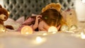 A little girl is lying alone on her stomack on a huge bed with her head lying face down and smiling, having teddybears Royalty Free Stock Photo