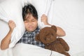 Little girl lying in bed covering head with pillow because too loud annoying noise Royalty Free Stock Photo