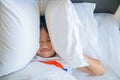 Little girl lying in bed covering head with pillow because too loud annoying noise