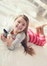 Little girl lying in bed with a remote control TV Royalty Free Stock Photo